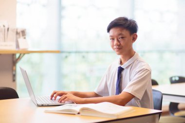 Okulda dizüstü bilgisayarı olan Asyalı bir çocuk. Sınıfta öğrenci. Kütüphanede bilgisayarla ödev yapan üniformalı bir genç. Genç çocuk ders çalışıyor. Çocuklar ders çalışır. Okula geri dön..