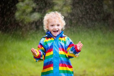 Gökkuşağı renkli yağmur altında oynarken su geçirmez ceket küçük sarışın kıvırcık çocuk. Çocuklar açık havada sonbahar duş eğleniyor.