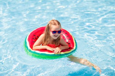 Yüzme havuzunda karpuz şişirilebilir yüzüğü olan bir çocuk. Küçük kız tropikal tatil köyü havuzunda yüzmeyi öğreniyor. Çocuk gözlüğü. Çocuklar için su oyuncakları ve şamandıralar. Çocuklar için sağlıklı spor. 