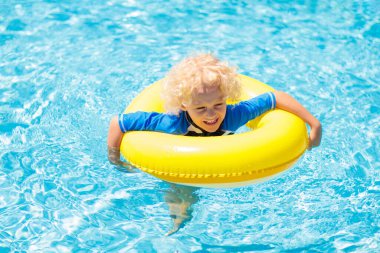 Yüzme havuzunda şişme yüzük takan çocuk. Sarışın kıvırcık çocuk yüzmeyi ve açık havuza dalmayı öğreniyor. Çocuklarla yüzmek. Çocuklar için sağlıklı yaz sporları aktivitesi. Güneş koruması. Su eğlencesi