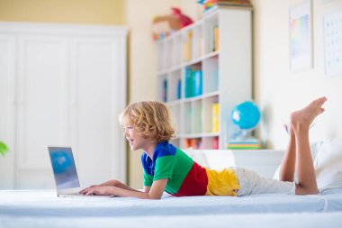 Bilgisayarda ödev yapan bir çocuk. Çevrimiçi sınıf. Evde eğitim ve uzaktan eğitim. Küçük okul çocuğu monitörde okuyor. Çocuklar video oyunu oynar. Oyun ve ekran zaman denetimi.