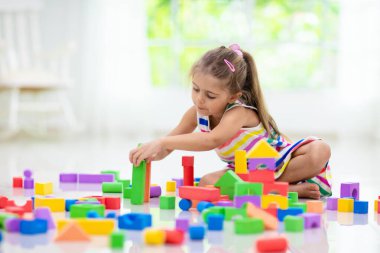 Kids play with colorful blocks. Little girl building tower at home or day care. Educational toy for young child. Construction creative game for baby or toddler kid. Mess in kindergarten playroom.