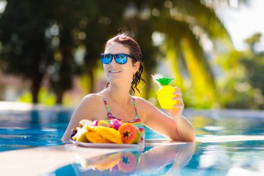 Yüzme havuzunda tropik meyve tabağı. Mango, ananas, portakal yiyen ve yaz tatilinde egzotik adada taze meyve suyu içen genç bir kadın. Sağlıklı beslenme. Plaj tatili ve yüzme eğlencesi.
