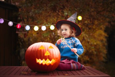 Çocuklar Cadılar Bayramı kostümüyle şeker mi şaka mı oynuyorlar. Banliyöde renkli elbiseli çocuklar şeker kovası ile geziyorlar. Küçük kız balkabağı feneriyle şeker mi şaka mı? Sonbahar tatili eğlencesi.