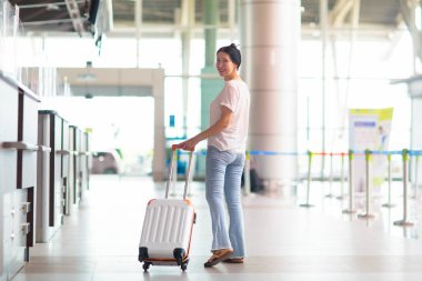 Havaalanındaki genç Asyalı kadın. Hava yoluyla seyahat et. Havaalanı terminalinde elinde pasaport ve uçuş kartıyla yürüyen bir kadın. Tatil ya da iş gezisi. Bavullu kız. Tatil uçuşu için giriş yap..