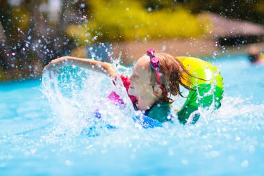 Yüzme havuzunda yüzen bir çocuk. Çocuklar yüzer. Genç çocuklar için renkli gökkuşağı yüzüyor. Küçük çocuk yaz tatilinde tropik tatil köyünde eğleniyor. Plaj ve su oyuncakları. Güneş koruması.