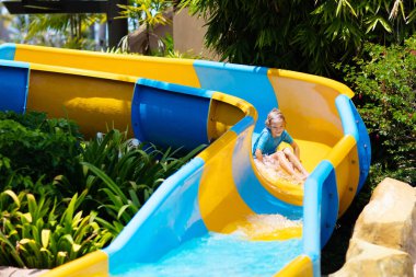 Su parkında su kayağı yapan çocuklar. Çocuklar yaz tatilinde tropik tatil köylerinde su kaydırağında eğleniyorlar. Islak çocuk ve bebek parkı olan eğlence parkı.