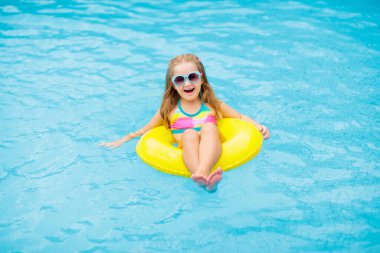 Yüzme havuzunda yüzen bir çocuk. Çocuklar yüzer. Küçük çocuklar için renkli sarı yüzer. Küçük kız yaz tatilinde tropikal tatil köyünde eğleniyor. Plaj ve su oyuncakları. Güneş koruması.