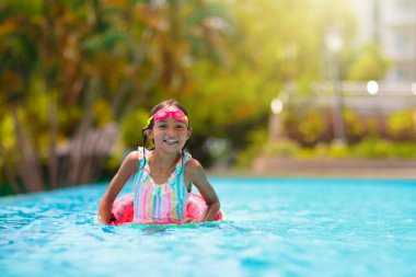 Yüzme havuzunda yüzen bir çocuk. Çocuklar yüzer. Genç çocuklar için renkli gökkuşağı yüzüyor. Küçük kız yaz tatilinde tropikal tatil köyünde eğleniyor. Plaj ve su oyuncakları. Güneş koruması.