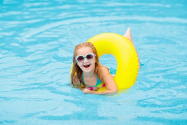 Yüzme havuzunda yüzen bir çocuk. Çocuklar yüzer. Küçük çocuklar için renkli sarı yüzer. Küçük kız yaz tatilinde tropikal tatil köyünde eğleniyor. Plaj ve su oyuncakları. Güneş koruması.