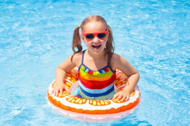 Yüzme havuzunda yüzen bir çocuk. Çocuklar yüzer. Küçük çocuklar için renkli sarı yüzer. Küçük kız yaz tatilinde tropikal tatil köyünde eğleniyor. Plaj ve su oyuncakları. Güneş koruması.