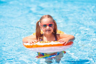 Yüzme havuzunda yüzen bir çocuk. Çocuklar yüzer. Küçük çocuklar için renkli sarı yüzer. Küçük kız yaz tatilinde tropikal tatil köyünde eğleniyor. Plaj ve su oyuncakları. Güneş koruması.