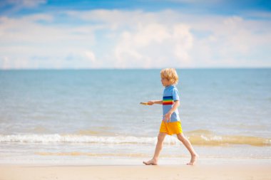 Tropik plajda oynayan bir çocuk. Deniz kıyısında elinde kova ve kürek olan küçük bir çocuk. Aile yaz tatili. Çocuk kumdan kale yapıyor. Çocuklar için su ve kum eğlencesi. Çocuklar oynar, okyanus kıyısında kale yaparlar.