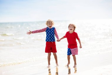 Çocuklar güneşli plajlarda Amerikan bayrağıyla koşuyor. 4 Temmuz kutlamaları. Bağımsızlık Günü 'nde Amerikan aile eğlencesi. Vatansever çocuklar Amerikan bayramını kutluyor. Amerika sembollü kız ve erkek..