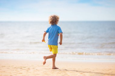 Tropik plajda oynayan bir çocuk. Deniz kıyısında elinde kova ve kürek olan küçük bir çocuk. Aile yaz tatili. Çocuk kumdan kale yapıyor. Çocuklar için su ve kum eğlencesi. Çocuklar oynar, okyanus kıyısında kale yaparlar.