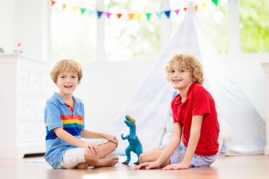 Çadırlı çocuk odası. Çocuklar beyaz güneşli yatak odasında oynarlar. Çocuk odası ya da oyun odası için rahat bir iç mekan. Oyuncak blokları olan küçük bir çocuk ve tahta zeminde oynayan bir dinozor. Ev dekorasyonu.
