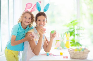 Anne ve çocuk Paskalya yumurtası renginde. Tavşan kulaklı küçük bir çocuk ve annesi yumurta boyuyor. Çocuklar için Paskalya yumurtası avı. Aile kutlaması ve bahar tatili için ev dekorasyonu..