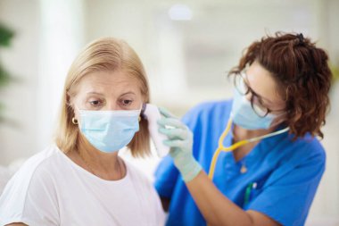 Doktor maske takan hasta hastayı muayene ediyor. Test ve tarama için sağlık kliniğindeki hasta kadın. Evde virüs tedavisi. Kadın öksürüyor, göğsünde ağrı var. Grip mevsimi. Pratisyen hekim..