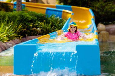 Su parkında su kayağı yapan çocuklar. Çocuklar yaz tatilinde tropik tatil köylerinde su kaydırağında eğleniyorlar. Islak çocuk ve bebek parkı olan eğlence parkı.