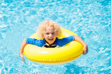 Yüzme havuzunda şişme yüzük takan çocuk. Sarışın kıvırcık çocuk yüzmeyi ve açık havuza dalmayı öğreniyor. Çocuklarla yüzmek. Çocuklar için sağlıklı yaz sporları aktivitesi. Güneş koruması. Su eğlencesi