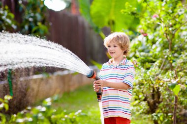 Bahçede çiçekleri ve bitkileri sulayan çocuk. Güneşli bahçesinde su hortumu olan bir çocuk. Küçük çocuk bahçeyle uğraşıyor. Evde yaz eğlencesi. Baharda aile aktivitesi. Çocuklar ebeveynlere yardım.