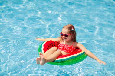 Yüzme havuzunda karpuz şişirilebilir yüzüğü olan bir çocuk. Küçük kız tropikal tatil köyü havuzunda yüzmeyi öğreniyor. Çocuk gözlüğü. Çocuklar için su oyuncakları ve şamandıralar. Çocuklar için sağlıklı spor. 