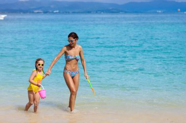 Anne ve çocuk tropikal kumsalda oynarken. Aile deniz yaz tatili. Anne ve çocuk kız oynamak ve kumdan kale inşa. Ebeveyn ve çocuklar için eğlence okyanus ve su. Zinde ve sağlıklı aile egzotik Plajı'nda.