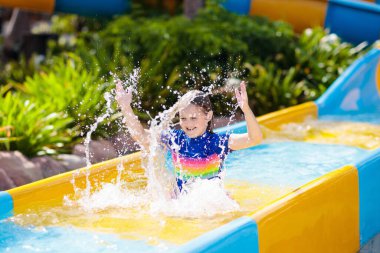 Su parkında su kayağı yapan çocuklar. Çocuklar yaz tatilinde tropik tatil köylerinde su kaydırağında eğleniyorlar. Islak çocuk ve bebek parkı olan eğlence parkı.