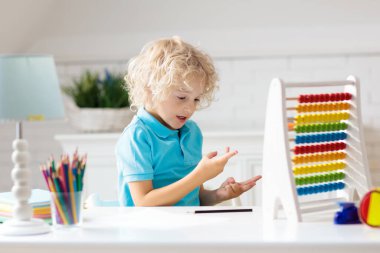 Çocuk evde ödev yapıyor. Ahşap renkli abaküsü olan küçük çocuk matematik egzersizi yapıyor toplama ve sayma yapıyor. Çocuklar çalışır ve öğrenir. Anaokulu çocuğu yazıp okuyor. Okula geri dön..