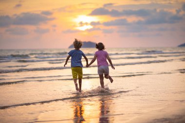 Okyanus sahilinde oynayan bir çocuk. Gün batımında dalgalara atlayan bir çocuk. Çocuklu aileler için deniz tatili. Küçük oğlan ve kız yaz tatilinde egzotik adada koşuyorlar..