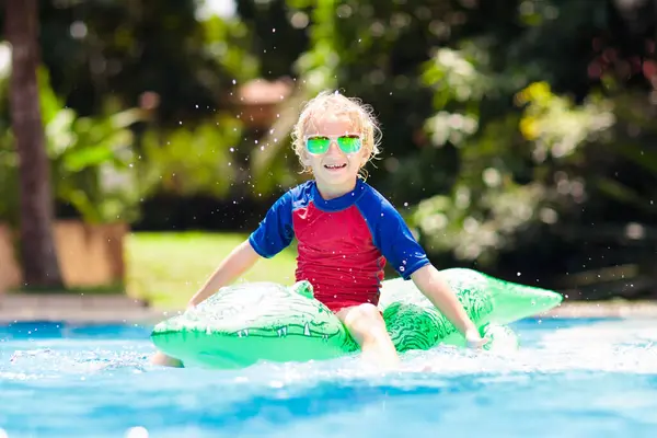 stock image Child playing in swimming pool. Kids learn to swim. Little baby boy with inflatable toy float playing in water on summer vacation in tropical resort. Kid with toy crocodile on beach holiday.