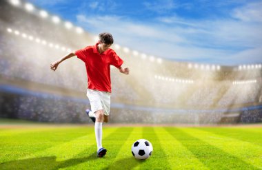 Stadyum sahasında futbolcu. Futbol maçı. Kırmızı tişörtlü ve beyaz şortlu genç adam dışarıda topa vuruyor. Koşan ve zıplayan bir sporcu. Şampiyonluk maçı zaferi.