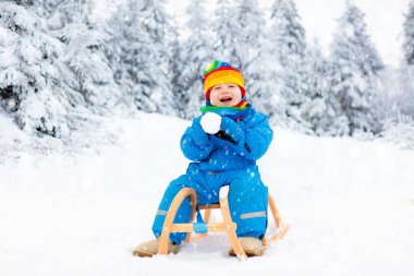 Küçük çocuk kızakla gezintiye çıkıyor. Çocuk kayağı. Kızak süren küçük bir çocuk. Çocuklar karda dışarıda oynarlar. Çocuklar kışın Alp dağlarında kızak kullanırdı. Aile Noel tatili için açık hava eğlencesi.