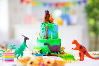 Çocukların doğum günü partisi. Dinozor temalı pasta. Küçük kız mumları üflüyor ve hediyeleri açıyor. Çocuk etkinliği. Dinazorlar için dekorasyon temalı kutlama.