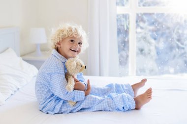 Kışın anne yatakta oynayan çocuklar. Çocuk kar beyaz yatak odasında uyan. Küçük çocuk mavi pijama. Noel pijama ve yatak çocuk ve bebek için. Aile karlı soğuk Xmas gün sabahı.