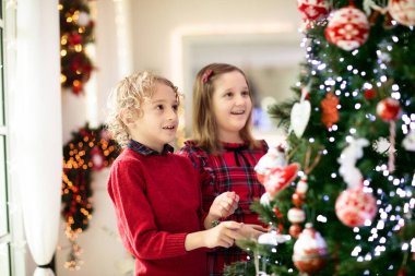 Evde Noel ağacı süsleyen çocuk. Xmas süsü takmış küçük bir kız ve oğlan. Çocuklu aile kış tatilini kutlar. Çocuklar Noel için oturma odasını ve şömineyi dekore ederler.. 