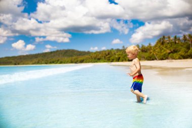 Tropik plajlarda palmiye ağaçlarıyla oynayan bir çocuk. Deniz kıyısındaki küçük erkek bebek. Aile yaz tatili. Çocuklar su ve kum oyuncaklarıyla oynuyor. Okyanus ve ada eğlencesi. Asya 'da küçük çocuklarla seyahat et..