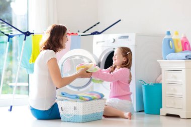 Anne ve çocuklar Çamaşırhane, çamaşır makinesi ile Oda veya kurutma. Aile işleri. Modern ev aygıtları ve çamaşır deterjan beyaz güneşli evinde. Raf kurutma üzerinde temiz yıkanmış kıyafetler. 