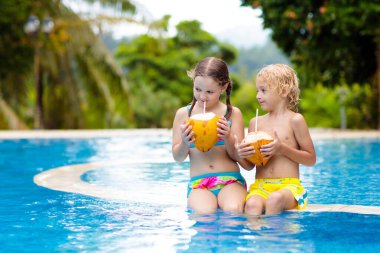 Açık havuzda hindistan cevizi içen çocuk. Çocuklar tropik tatil köylerinde yüzerler. Çocuklar için sağlıklı egzotik meyve ferahlatıcı. Genç bir çocukla seyahat et. Kumsal ve su eğlencesi. Yaz aile tatili.