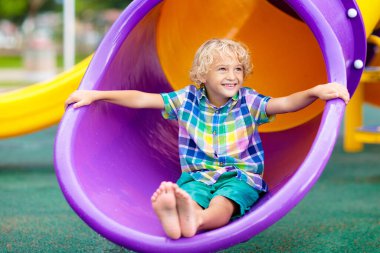 Çocuk dışarıda oyun oynuyordu. Çocuklar okulda ya da anaokulunda oynarlar. Aktif çocuk renkli kayıyor ve sallanıyor. Çocuklar için sağlıklı bir yaz aktivitesi. Küçük çocuk dışarı tırmanıyor..
