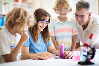 Okul fen dersi. Kimya dersindeki öğrenciler. Çocuklar kimyasal reaksiyonu izliyor. Öğretmen ve ilkokul çocukları sınıfta. Birinci sınıf çocuk bilimsel deney yapıyor. Kök kulüp.