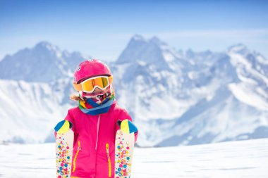Çocuk dağlarda kayak yapıyor. Güvenlik kaskı, gözlüğü ve direkleri olan aktif bir çocuk. Küçük çocuklar için kayak yarışı. Aile için kış sporu. Alp okulunda çocuklar kayak dersi alıyor. Küçük kayakçı karda yarışıyor