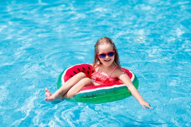 Yüzme havuzunda karpuz şişirilebilir yüzüğü olan bir çocuk. Küçük kız tropikal tatil köyü havuzunda yüzmeyi öğreniyor. Çocuk gözlüğü. Çocuklar için su oyuncakları ve şamandıralar. Çocuklar için sağlıklı spor. 