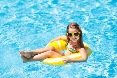 Havuzda yüzen çocuk şişme sarı limon halkası takıyor. Küçük kız turuncu yüzgeçle yüzmeyi öğreniyor. Bebek ve bebek için su oyuncağı. Çocuklar için sağlıklı bir açık hava sporu. Çocuklar plaj eğlencesi.  