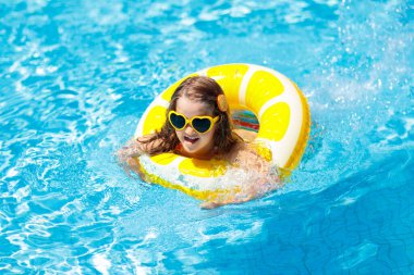 Havuzda yüzen çocuk şişme sarı limon halkası takıyor. Küçük kız turuncu yüzgeçle yüzmeyi öğreniyor. Bebek ve bebek için su oyuncağı. Çocuklar için sağlıklı bir açık hava sporu. Çocuklar plaj eğlencesi.  