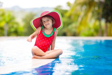 Yüzme havuzunda bir çocuk. Çocuklu aileler için tropik bir tatil. Kırmızı mayo ve karpuz şapkalı küçük bir kız egzotik adalarda açık havuzda oynuyor. Çocuklar için su ve yüzme eğlencesi