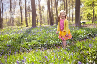 Bluebells çocukla. Mor bluebell çiçekli güzel bahar orman oynayan güzel elbiseli küçük kız. Park blue Bell'de çiçek çayır ile çocukları. Doğa keşfetmek iskambil.