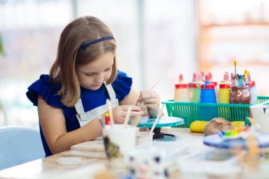 Çömlek çiletmek için çalışan çocuk. Atölyede çocuk sanatları ve el sanatları sınıfı. Küçük kız kil fincan ve kase oluşturma. Okulda küçük çocuklar için yaratıcı etkinlik. Seramik ile oyuncak oluşturan sevimli çocuk. 