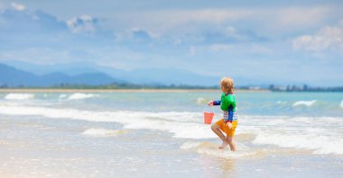 Tropik sahilde oynayan çocuk. Küçük çocuk kazma kum deniz desteklemek. Aile yaz tatili. Çocuklar su ile oynamak ve oyuncakları kum. Okyanus ve Adası eğlenceli. Küçük çocuklarla seyahat. Asya tatil.