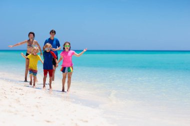 Aile yaz tatili. Anne baba ve çocuklar tropik plajda. Anne ve çocuklar adanın okyanus kıyısında oynuyorlar. Temiz suda beyaz kumlar üzerinde koşuyorlar. Küçük çocukla tatildeyiz. Çocukla seyahat et..